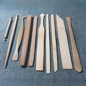 以下が含まれることがあります： さまざまな木製の陶器用具のコレクション。リブツール、モデリングツール、ニードルツールなど。ツールは明るい木材と暗い木材でできており、青色のテクスチャのある表面に配置されています。粘土の成形と細部へのこだわりに使用します。
