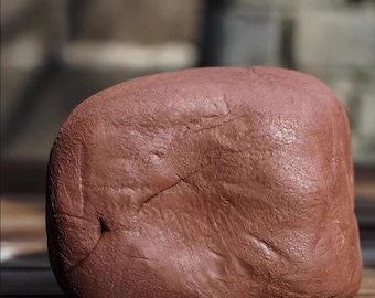 May include: A reddish-brown, smooth, rounded rock with a slightly irregular shape. The rock has a few visible cracks and a textured surface. The image is a close-up shot of the rock.