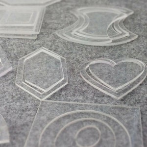 Peut inclure: Un ensemble de pochoirs en plastique transparent de différentes formes, notamment un cœur, un hexagone et un cercle. Les pochoirs sont superposés, créant un effet multidimensionnel.