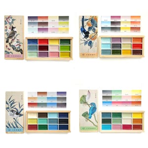 May include: Watercolor paint sets with wooden boxes and color charts. Each set includes a rectangular wooden box with 12 watercolor paints, a color chart, and a decorative card with a bird illustration. The color palettes vary, offering a range of hues.