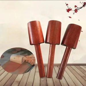 Puede incluir: Tres mazos de madera de color marrón rojizo se muestran sobre un fondo claro. Cada mazo tiene una cabeza cilíndrica y un mango largo y delgado. Una pequeña imagen muestra un mazo en uso.