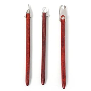 May include: Three wood-handled tools with metal tips. The tools have a dark reddish-brown finish and are arranged vertically against a white background. The tips have different shapes, including a curved blade, a loop, and a rounded scoop.