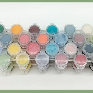 K&ouml;nnte beinhalten: Ein Set aus 24 Farbt&ouml;pfen in verschiedenen Farben, darunter Gr&uuml;n, Orange, Blau, Rosa und Lila. Die Farbt&ouml;pfe sind in einer transparenten Kunststoffschale angeordnet, ideal f&uuml;r Malprojekte. Jeder Topf ist mit einem anderen Farbton gef&uuml;llt.