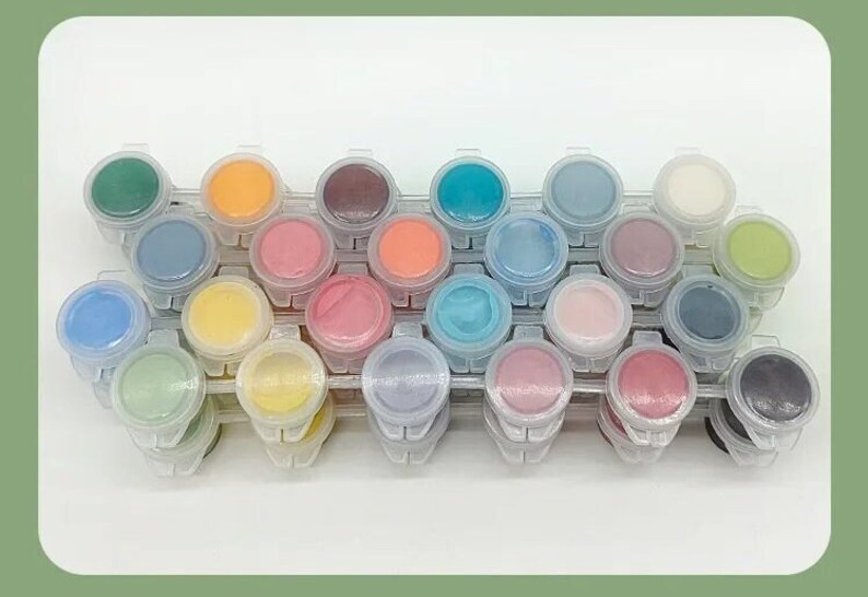 K&ouml;nnte beinhalten: Ein Set aus 24 Farbt&ouml;pfen in verschiedenen Farben, darunter Gr&uuml;n, Orange, Blau, Rosa und Lila. Die Farbt&ouml;pfe sind in einer transparenten Kunststoffschale angeordnet, ideal f&uuml;r Malprojekte. Jeder Topf ist mit einem anderen Farbton gef&uuml;llt.