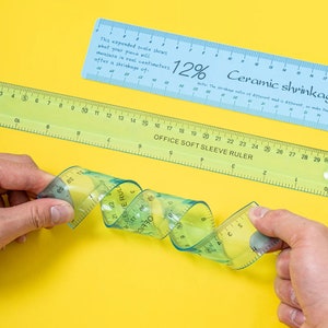 May include: A close-up of a flexible ruler that is curled into a spiral shape. The ruler is transparent blue and green with white markings. The ruler is labeled "OFFICE SOFT SLEEVE RULER".