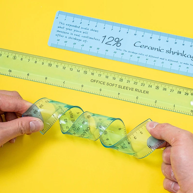 May include: A close-up of a flexible ruler that is curled into a spiral shape. The ruler is transparent blue and green with white markings. The ruler is labeled "OFFICE SOFT SLEEVE RULER".