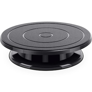 May include: A black, rotating display stand with a circular top and base. The top surface has a textured, matte finish with concentric circles. The base is glossy black, and the stand is designed to showcase products.
