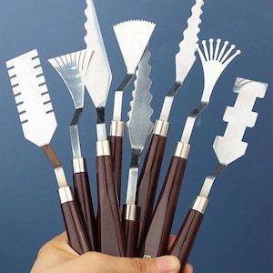 May include: A set of nine painting tools with brown wooden handles and various metal blades. The blades have different shapes and sizes, including a fan, a comb, and a pointed tip.