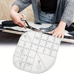 May include: A clear, curved quilting ruler with black markings and measurements is being used with scissors to cut fabric. The ruler has labeled sections for different radius corners. The fabric is black and white.