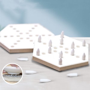 May include: A white hexagonal game board with a brown border and white pegs. The board has multiple holes and the pegs can be placed in the holes. There are several pegs scattered around the board.