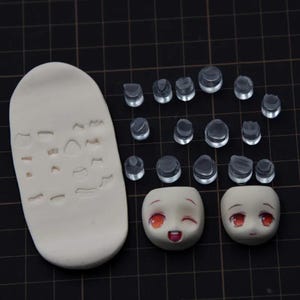 May include: A white silicone mold with various shapes for sculpting, along with clear plastic stamps and two painted doll faces with red eyes and smiling expressions.