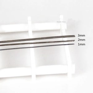 以下が含まれることがあります： 白い表面に、1mm、2mm、3mmの異なるサイズの金属棒が3本並べて置かれています。棒はすべて同じ色で、濃い灰色です。