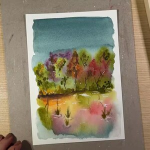 May include: Watercolor painting of a landscape with a teal sky, colorful trees, and a reflective body of water. The trees feature shades of green, red, and orange. The water reflects the colors of the trees and sky, with hints of pink and yellow.