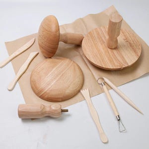 Może przedstawiać: Zestaw drewnianych narzędzi do rzeźbienia gliny, w tym narzędzie w kształcie grzyba, narzędzie okrągłe z uchwytem i różne narzędzia do rzeźbienia. Narzędzia są ułożone na brązowej powierzchni papieru.