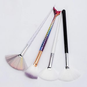 May include: Four make-up brushes with fan-shaped bristles. One brush has a white, twisted handle and a silver ferrule. Another has a rainbow-coloured mermaid tail handle. The other two brushes have white and black handles.