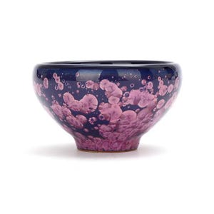 Può includere: Una piccola ciotola in ceramica blu scuro con una glassa screziata rosa e viola. La ciotola ha una forma arrotondata e un bordo leggermente svasato.