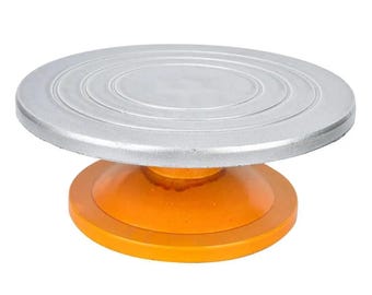 May include: A silver cake turntable with a smooth, circular top and a bright orange base. The turntable is designed to rotate smoothly for decorating cakes and other pastries.