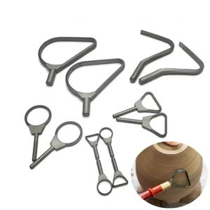 Puede incluir: Una colección de varias herramientas de cerámica grises, que incluyen herramientas de bucle, herramientas de cinta y una herramienta de recorte. Las herramientas están dispuestas sobre una superficie blanca, con una herramienta en uso en una pieza de cerámica marrón.