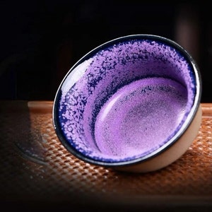 Può includere: Una piccola tazza da tè in ceramica di colore viola e blu con una glassa macchiettata.