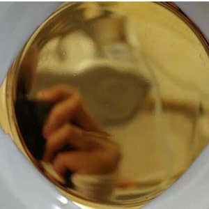 Puede incluir: Primer plano de un objeto redondo de metal de color dorado. El objeto es liso y brillante, reflejando la luz.