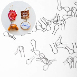Peut inclure: Gros plan sur un ensemble de crochets d'oreille en argent. Les crochets sont petits et délicats, avec une boucle en haut et une petite pointe en bas. Il y a 20 crochets au total.
