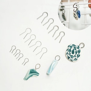 Peut inclure: Un ensemble de joncs de saut argentés avec une variété de breloques en pâte polymère faites à la main. Les breloques sont dans des tons de bleu et de vert avec des motifs floraux et abstraits.