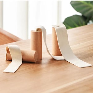 Può includere: Tre ganci da parete in legno con cinturini in tessuto bianco. I ganci sono cilindrici e hanno una finitura in legno naturale. I cinturini sono attaccati ai ganci e possono essere utilizzati per appendere oggetti.