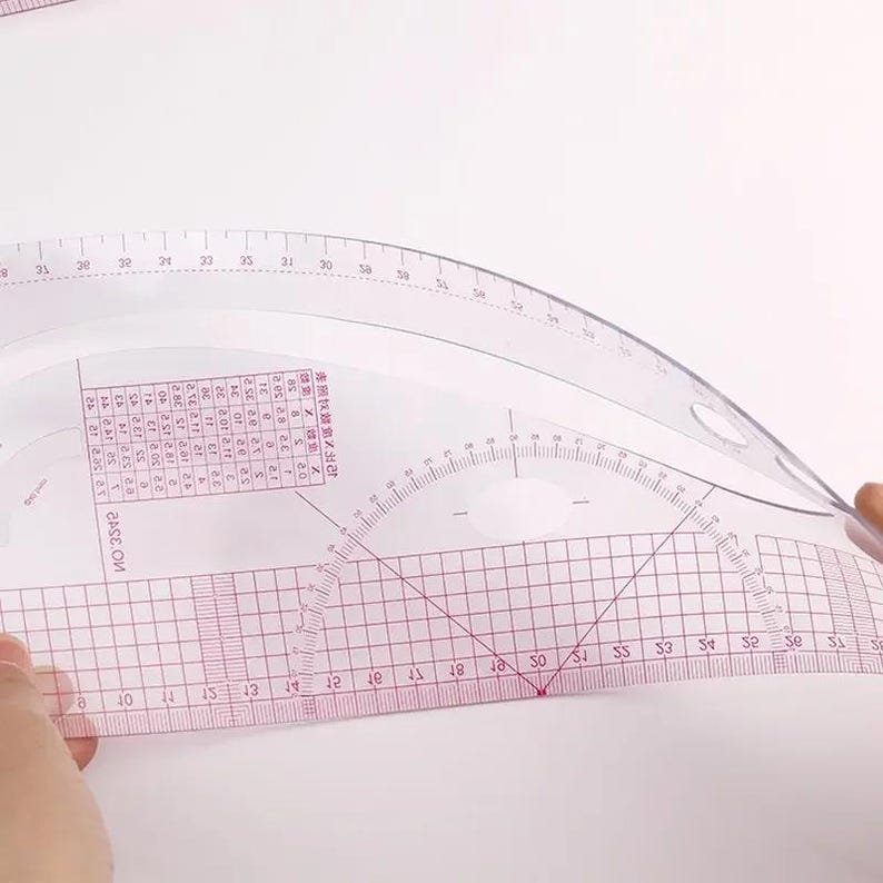 May include: Clear plastic sewing pattern rulers with red grid lines and measurement markings. The rulers are curved and straight, with numbers and text printed on them. The image shows a close-up of the rulers.