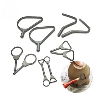 May include: A collection of gray pottery tools, including loop tools, ribbon tools, and a curved trimming tool. The tools are arranged on a white surface, with one tool in use on a clay pot.
