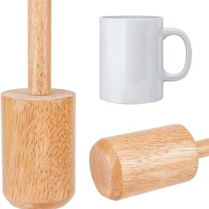 May include: The image shows a wooden mallet and a white ceramic mug. The mallet is made of light-coloured wood and has a cylindrical head and handle. The mug is plain white with a curved handle, suitable for hot beverages.