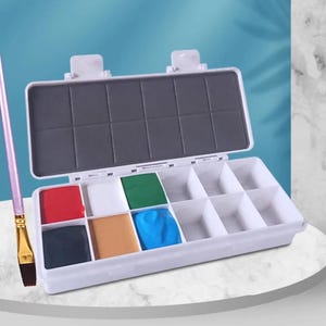 May include: A white plastic watercolor paint palette box with a hinged lid and ten rectangular compartments. Five compartments are filled with solid paint in red, white, green, tan, and blue. A single paintbrush with a light purple handle is included.