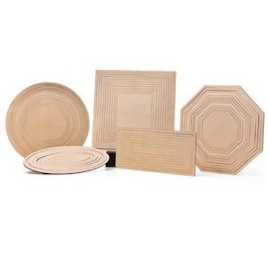 May include: A collection of unfinished light-coloured wooden shapes including a large circle, a smaller oval, a square, a rectangle, and an octagon. Each piece features concentric engraved lines creating a layered, nested appearance on the flat surface.