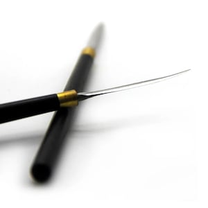 May include: A close-up of two black and gold tools with silver blades. One tool is in the foreground, with a curved blade. The other tool is in the background, with a straight blade. Both tools have a black handle with gold accents.