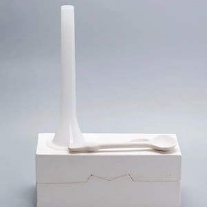 Puede incluir: Un juego de utensilios de cocina de cerámica blanca, que incluye un embudo alto, una cuchara y una caja rectangular. El embudo es cilíndrico con una base acampanada. La cuchara tiene un cuenco redondeado y un mango largo. La caja tiene un corte en zigzag.