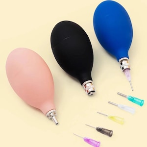 Puede incluir: Tres jeringas de bulbo de goma en rosa, negro y azul, cada una con una punta de metal. También se muestran varias puntas de colores. Las jeringas se utilizan para diversas aplicaciones de laboratorio o médicas.