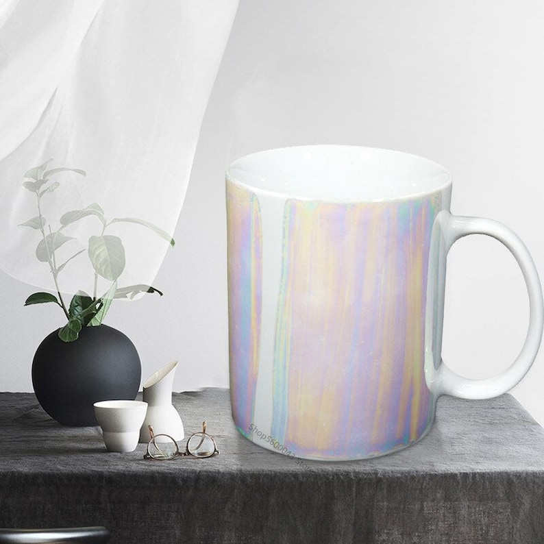 May include: A white ceramic mug with a iridescent finish. The mug has a handle and is sitting on a gray surface.