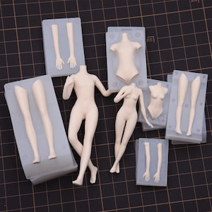 May include: A selection of beige doll body parts, including arms, legs, torsos, and hands, are shown. The parts are in clear plastic moulds, with two complete doll figures in the centre. The background is a dark grid.