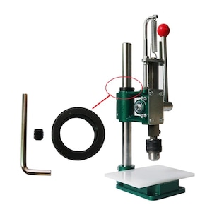 Puede incluir: Una prensa de metal verde con una plataforma blanca, un anillo negro, una llave inglesa plateada y un pequeño tornillo plateado. La prensa tiene una varilla plateada con un anillo negro en la parte superior.