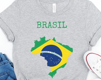 May include: A gray t-shirt with the word "BRASIL" printed in green letters and a green, yellow, and blue outline of the country of Brazil with the words "ORDEM E PROGRESSO" printed inside the outline.