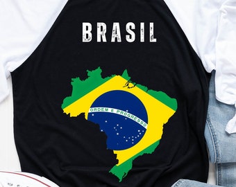 May include: Black and white baseball style t-shirt with a white and green outline of the country of Brazil with the words "Brasil" and "Ordem e Progresso" on it. The shirt has white sleeves.