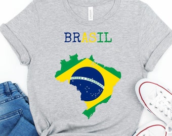 May include: A gray t-shirt with the word "BRASIL" in blue and yellow letters and a green and yellow outline of Brazil with the Brazilian flag inside. The shirt is paired with blue jeans and white sneakers.