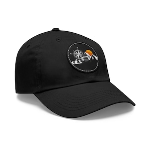 May include: Black baseball cap with a circular patch featuring a compass, a mountain range, a setting sun, and a vehicle. The patch has a white stitched border.