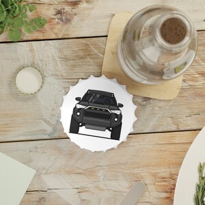 Könnte beinhalten: Ein weißer Flaschenverschluss mit einer schwarzen und grauen Illustration eines Autos. Das Auto hat einen schwarzen Kühlergrill und Scheinwerfer.