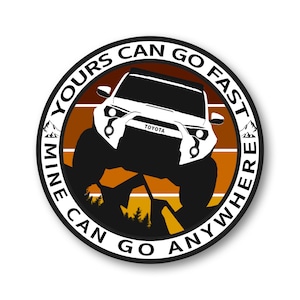 May include: A circular sticker featuring a white Toyota SUV with the text "MINE CAN GO ANYWHERE, YOURS CAN GO FAST". The design includes a mountain range and a sunset-like background.