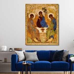 May include: A rectangular wall art print featuring a reproduction of the Holy Trinity icon. The artwork depicts three winged figures with halos seated around a table with a central chalice, rendered in shades of gold, blue, and deep red.