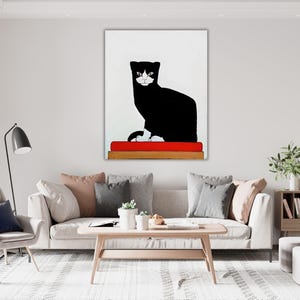 May include: A rectangular wall art print featuring a stylized black cat with white facial markings and white paws. The cat is sitting on a solid red rectangular cushion, which is placed on a wooden base, all set against a plain white background.