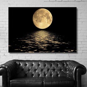 Op de afbeelding: Een rechthoekige wandkunstprint met een volle maan tegen een effen zwarte achtergrond. De maan toont gedetailleerde kraters en een gouden tint, waarbij het licht reflecteert in glinsterende patronen op het donkere water.