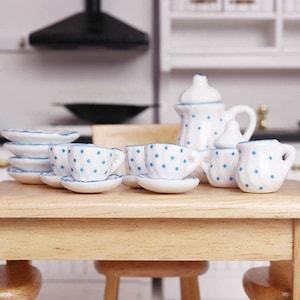 May include: A miniature white tea set with blue polka dots. The set includes a teapot, creamer, sugar bowl, four cups, and four saucers. The tea set is arranged on a wooden table.