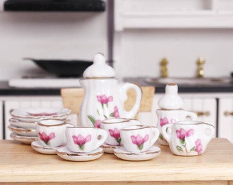 May include: A miniature porcelain tea set with a white base and pink floral designs. The set includes a teapot, creamer, sugar bowl, and four teacups and saucers.