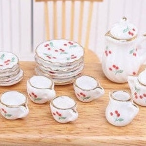 Peut inclure: Un service à thé miniature avec un motif de cerises. L'ensemble comprend une théière, un pot à crème, un sucrier et quatre tasses à thé et soucoupes. L'ensemble est en porcelaine blanche avec une bordure dorée.